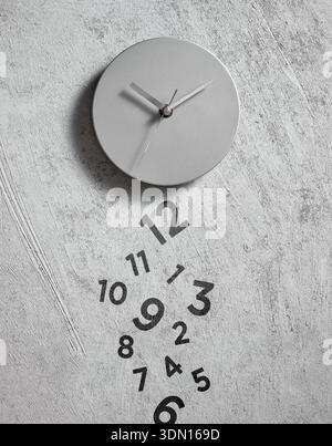 Minimalistische graue Uhr an einer strukturierten Wand, die Zahlen fallen vom Gesicht und symbolisieren das Verstreichen der Zeit und Fristen Stockfoto
