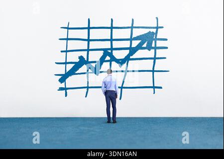 Geschäftsmann analysiert manuell gezeichnetes Diagramm mit aufsteigendem Trend auf einer weißen Wand, das den finanziellen Erfolg und die Zukunftsvision darstellt Stockfoto
