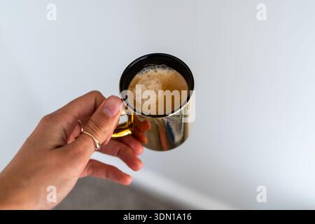 Die Frauenhand hält eine Tasse Cappuccino mit Schaumschaum auf einem sauberen weißen Hintergrund – minimalistisch, Platz für Text Stockfoto