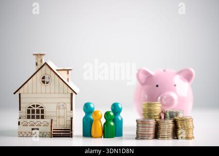 Hypothekensparnis und Familienfinanzplanungskonzept für den Immobilienkauf, mit Miniatur-Holzhaus, farbenfrohen Figuren, Münzstapeln und rosa Stockfoto