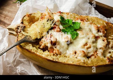 Seitenansicht von gebackenem Spaghetti-Kürbis oder Gemüsespaghetti gefüllt mit Hackfleisch und Käse, serviert in der Schale. Hausgemachtes Gericht auf rustikalem Holz. Stockfoto