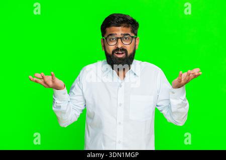 Indischer Mann zuckt Schultern hebt beide Hände mit einem verwirrten Blick auf das Gesicht, was Unsicherheit oder Verwirrung ausdrückt schwierige Wahl unerwartetes Ergebnis. Araber auf Chroma Key mit nachdenklichem Ausdruck Stockfoto