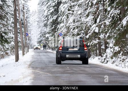 Auto fährt auf einer frostigen Landstraße durch schneebedeckten Fichtenwald an kalten Wintertagen. Stockfoto