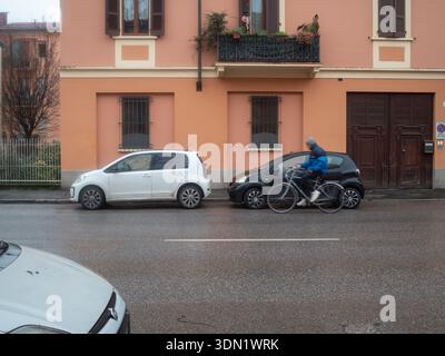 Cremona, Italien, 6. Februar 2026 urbane Straßenszene mit einem Radfahrer, der an einem Wohngebäude vorbeifährt, an dem parkenden Volkswagen und Toyota Aygo-Autos vorbeifahren Stockfoto