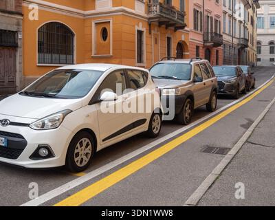 Cremona, Italien 6. Februar 2026 Fahrzeuge parkten entlang einer farbenfrohen europäischen Straße mit gelben Linien, die kompakte Fließhaken und SUVs gegen alte F Stockfoto