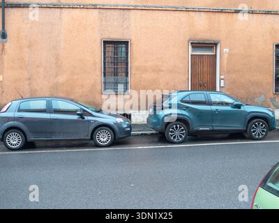 Cremona, Italien 6. Februar 2026 Fiat Punto und Toyota Yaris Cross parkten an einem Stadtrand, kompakte Autos vor einer verwitterten Stadtfassade, jeden Tag Stockfoto