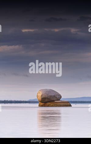 Ein Felsbrocken auf einem Felsen im ruhigen Ozean mit Reflexion unter grauem, bewölktem Morgenhimmel am Quintell Beach, Cape York, Lockhart River, Queensland Stockfoto