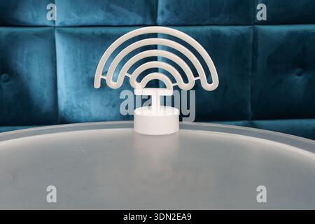Das WLAN-Symbol befindet sich auf einem transparenten Tisch in einem Café mit blauen Sitzgelegenheiten. Die Umgebung ist hell und einladend für Kunden. Stockfoto