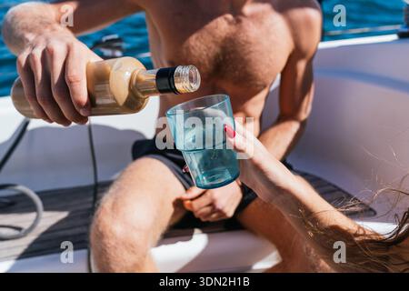 Mann, der Alkohol aus der Flasche in das Glas der Frau auf einem Segelboot gießt Stockfoto