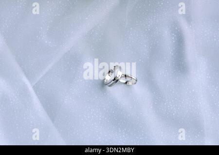 Elegantes Hochzeits-Flat-Lay mit Ringen auf weißem Stoff Stockfoto