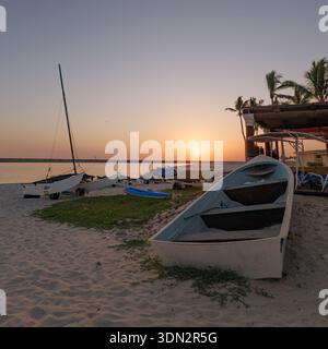 Eine ruhige, goldene Stunde Sonnenuntergang am Hawana Salalah Beach in Oman, mit einem kleinen Segelboot und Ruderboot, das auf dem Sand an Land gezogen wird. Die untergehende Sonne Stockfoto