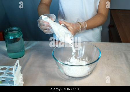 Nahaufnahme von Handschuhen, die eine weiße Substanz in eine Glasschale gießen. Stockfoto