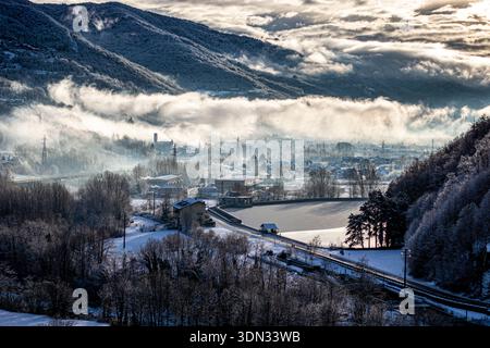 Nebel, der durch ein schneebedecktes Bergtal während des kalten Wintervormittags rollt Stockfoto
