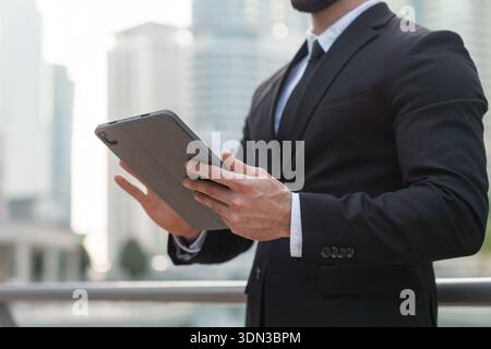 Geschäftsmann im formellen Anzug checkt Tablets in Dubais Stadtlandschaft umgeben von Wolkenkratzern. Stockfoto