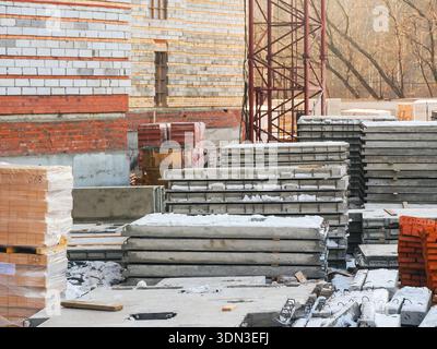 Eine Baustelle mit Stapeln von Betonplatten, Ziegeln und Baumaterialien, die einsatzbereit sind. Der Kran steht im Hintergrund. Stockfoto