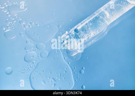 Tropfen von klarem flüssigem Serum mit Blasen auf blauen Hintergrund Stockfoto