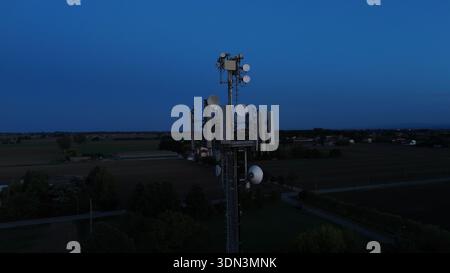 Mobilfunkturm steht vor dem dunkelblauen Himmel, ausgestattet mit verschiedenen Antennen für drahtlose Kommunikation und Mobilfunkdienste im gesamten Po Val Stockfoto