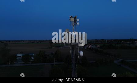 Mobilfunkturm steht vor dem dunkelblauen Himmel, ausgestattet mit verschiedenen Antennen für drahtlose Kommunikation und Mobilfunkdienste im gesamten Po Val Stockfoto