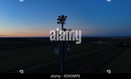 Mobilfunkturm steht vor dem dunkelblauen Himmel, ausgestattet mit verschiedenen Antennen für drahtlose Kommunikation und Mobilfunkdienste im gesamten Po Val Stockfoto