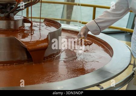Der Küchenchef glättet Schokolade. Einheitliches, glänzendes Schokoladenfinish. Der Küchenchef poliert gekonnt die Oberfläche von glänzend temperierter Schokolade Stockfoto
