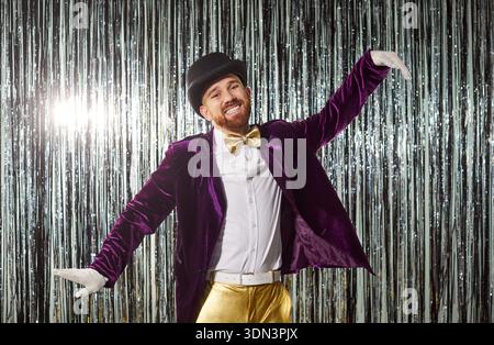 Fröhlicher Showman in lila Samtjacke und goldener Bowtie auf der glitzernden Lametta-Bühne Stockfoto