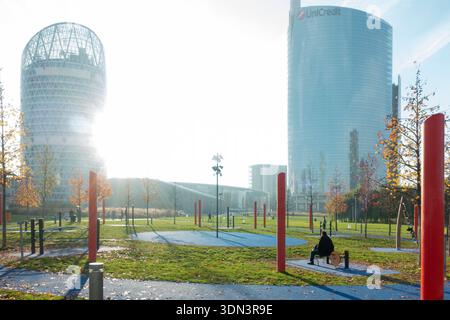 Moderne Wolkenkratzer reflektieren helle Sonne über einem städtischen öffentlichen Park mit sportlichen Menschen, Mailand, Italien Stockfoto