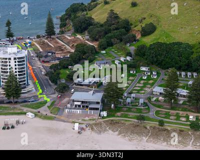 Blick aus der Vogelperspektive auf das kontrastreiche Blau des Meeres, das auf den weichen beigefarbenen Sand und die üppigen grünen Hügel trifft, Mount Maunganui, Neuseeland. Stockfoto