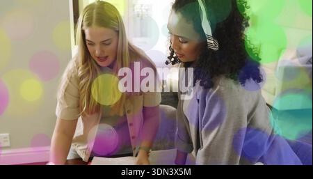 Zwei Frauen in Button-up und Strickjacke, die zu Hause Papiere lesen, mit farbenfrohem Bokeh Stockfoto