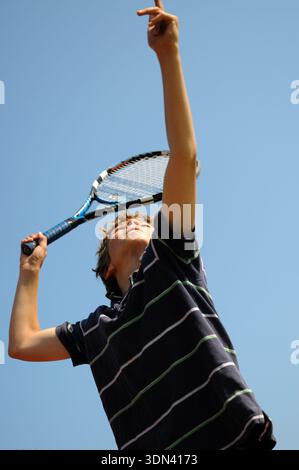 Junge, der im Freien Tennisball auf Vancouver Island, British Columbia, Kanada serviert, Action-Sport-Moment vor klarem blauem Himmel. Stockfoto