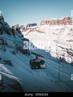 Blick auf eine Seilbahn steigt durch die klare, schneebedeckte Landschaft vor der Kulisse der majestätischen, sonnenverwöhnten Berge, Località Passo Sella, Trenti Stockfoto