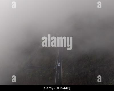 Aus der Vogelperspektive eines einsamen Autos, das sich durch eine Straße schlängelt, die von dichtem Nebel bedeckt ist, El Teide, Teneriffa, Spanien. Stockfoto