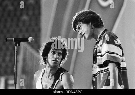 Dieses fesselnde Schwarz-weiß-Foto aus dem Jahr 1982 fängt einen dynamischen Moment zwischen Mick Jagger und Keith Richards von den Rolling Stones auf der Bühne in Rotterdam ein. Jagger neigt sich mit seiner charakteristischen Intensität zu Richards, der mit seinem Gitarrenriemen und einem Mikrofonständer in der Nähe zu sehen ist. Das Bild verkörpert perfekt die rohe Energie und die Verbindung des legendären Rockduos während einer Live-Performance. Stockfoto