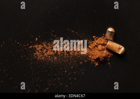Kapsel mit braunem Pulver auf schwarzem Hintergrund zum Thema Medikamente, Nahrungsergänzungsmittel, Behandlung und Vitamine Stockfoto