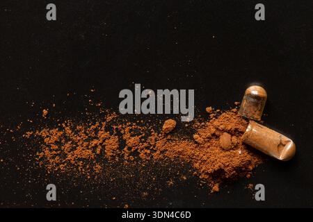 Kapsel mit braunem Pulver auf schwarzem Hintergrund zum Thema Medikamente, Nahrungsergänzungsmittel, Behandlung und Vitamine Stockfoto