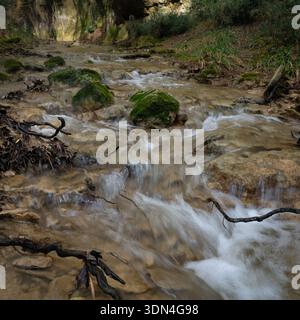 Verschwommener Wasserstrom, der über Felsen mit grünem Moos fließt. Stockfoto