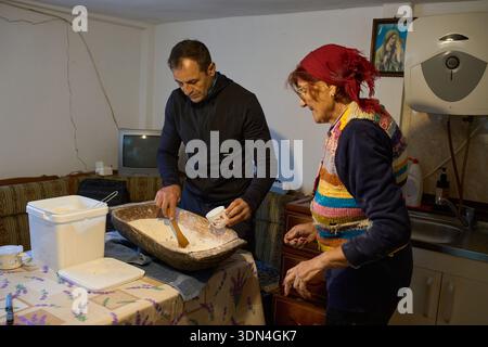 Mann mittleren Alters, der älteren Mutter hilft, Brotteig in traditionellem Holztrog zu Hause zu kneten Stockfoto