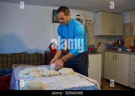 Mann mittleren Alters, der Brotteig auf einem Küchentisch knete, der mit Mehl bedeckt war Stockfoto