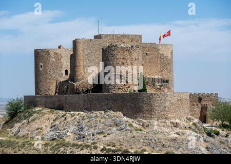 Eine historische Burg auf einem felsigen Hügel, mit runden Türmen und einer Steinmauer, mit Fahnen, die oben unter klarem blauen Himmel fliegen Stockfoto