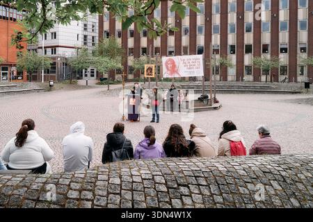 Eine Gruppe von Menschen sitzt auf einem Stein und beobachtet einen Redebeitrag. Es gibt eine kleine Bühne mit einem Banner. Nynashamn, Stockholmer County, Schweden, 10. Mai 2025. Stockfoto