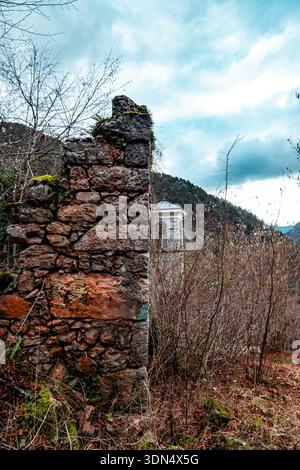 Alte Steinmauer Ruine in Waldlandschaft mit Bergen und wolkenblauem Himmel Stockfoto