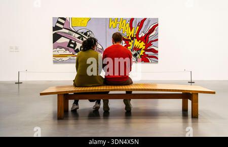 Ein Mann und eine Frau sitzen auf einer hölzernen Bank und sehen den Whaam! 1963, Roy Lichtenstein in der Tate Gallery in London, Großbritannien. Stockfoto