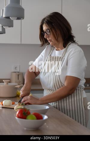 Frau, die Zwiebel auf der Küchenzeile hackt, mit selektivem Fokus auf Frau. Zubereitung von Speisen und tägliche Hausmannskost. Stockfoto