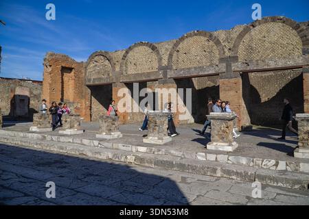 Ruinen des archäologischen Parks Pompeji, Italien. Die antike römische Stadt wurde 79 n. Chr. vom Vesuv zerstört. Touristen spazieren entlang erhaltener römischer Straßenpflaster. Stockfoto