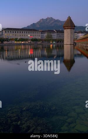 Der historische Kapellbrücke und die umliegenden Gebäude spiegeln sich im ruhigen Wasser des Vierwaldstättersees wider, wenn die Sonne hinter dem Pilatus untergeht Stockfoto