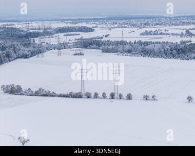 Breite schneebedeckte Felder mit Stromleitungen und kleine Dörfer am Horizont bei kaltem Wetter, Umspannwerk, Jettingen, Deutschland Stockfoto