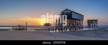 Pfahlhäuser bei Ebbe am Strand bei Sonnenuntergang, St. Peter-Ording, Nationalpark Schleswig-Holsteinisches Wattenmeer, Schleswig-Holstein, Deutschland Stockfoto