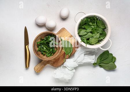 Sieb mit frischen Spinatblättern und Eiern auf hellem Hintergrund Stockfoto