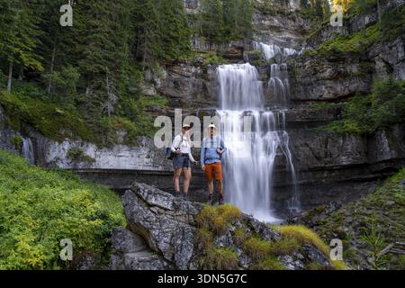 Zwei Wanderer stehen auf Felsen vor dem Cascata di Mezzo Wasserfall, lange Exposition, Vallesinella, Brenta, Trentino, Italien Stockfoto