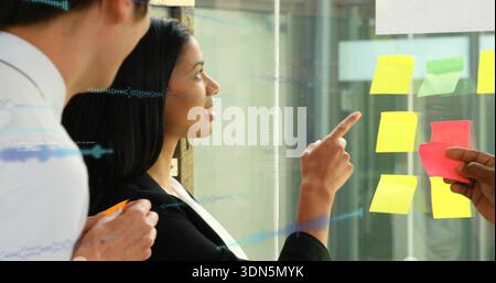 Zeigende Frau in schwarzem Blazer, die die Planung im Büro mit Notizen auf Glas führt, weiß-Hemd beobachtet Stockfoto