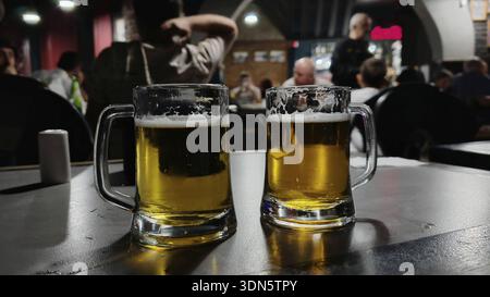 Zwei Biergläser auf einem Tisch in einer Bar mit Leuten im Hintergrund in der Abenddämmerung, Georgia Stockfoto